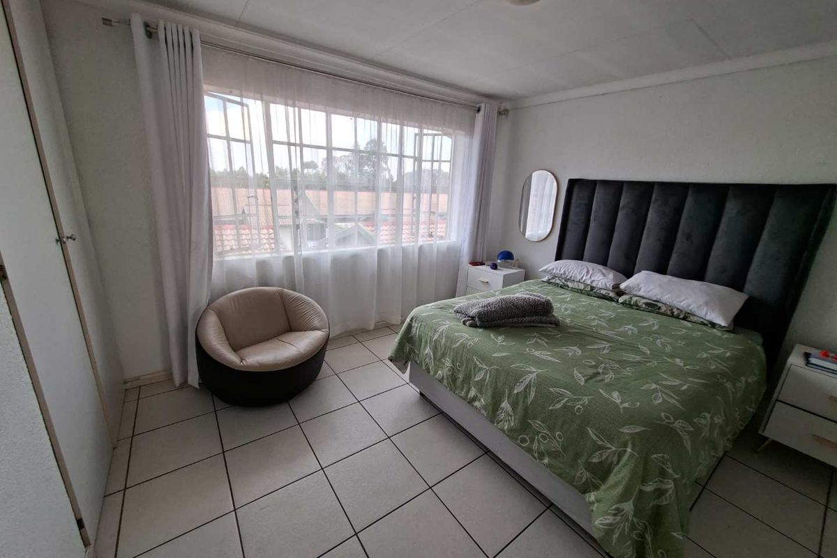 A bedroom featuring tiled flooring, a built-in cupboard, and a large window providing natural light.
