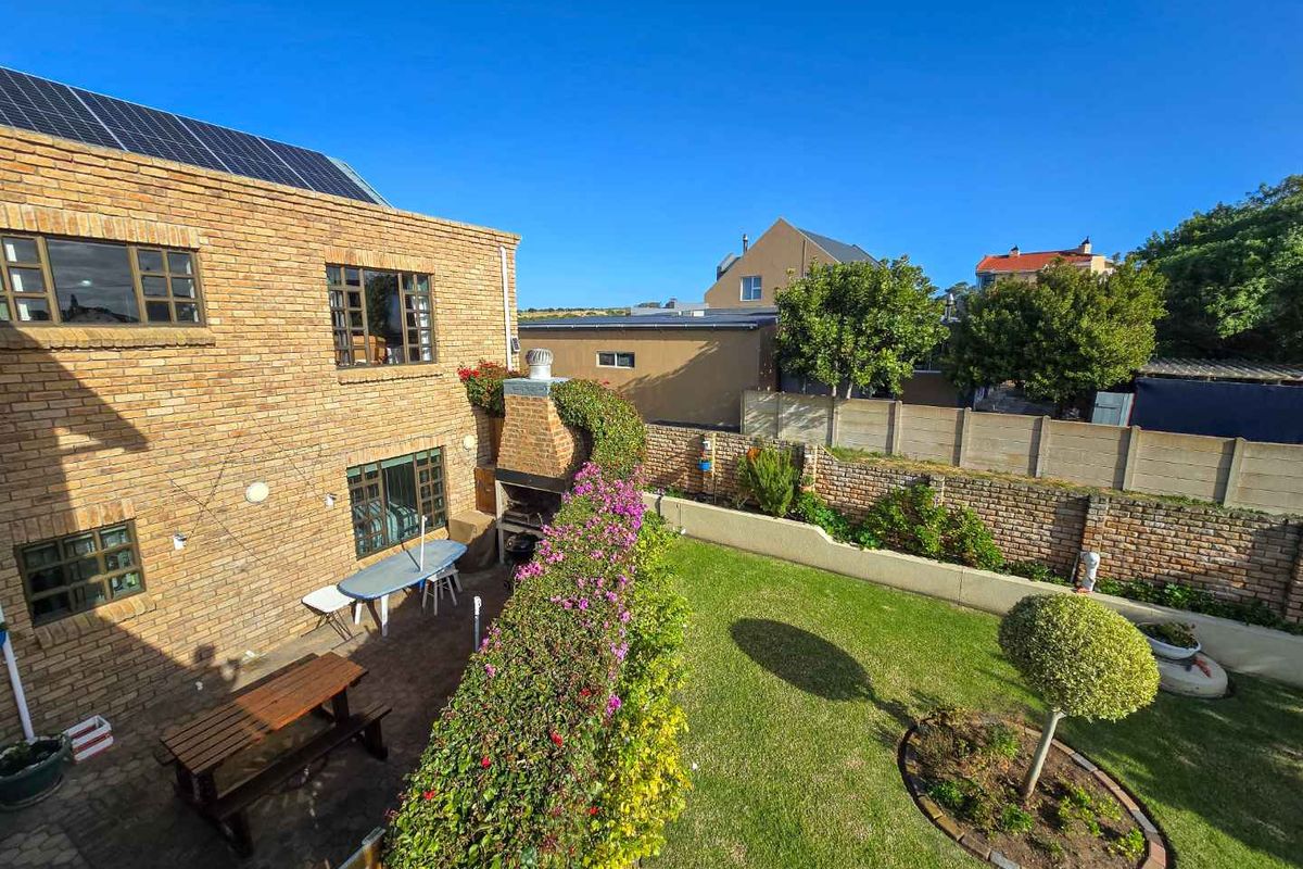 A rear garden view featuring a brick-built outdoor fireplace, paved patio area, and a well-maintained lawn with established landscaping.
