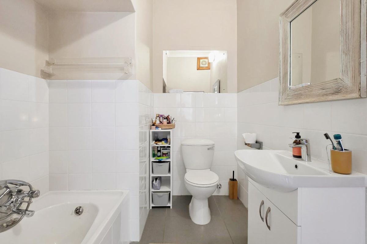 A clean and functional bathroom featuring a built-in bathtub, vanity basin with storage cabinet, and neutral ceramic tiling throughout.