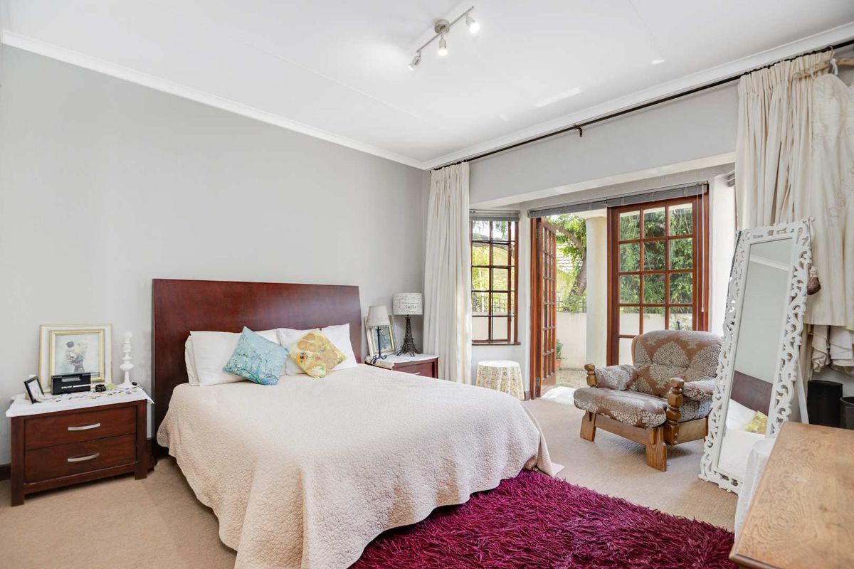 A spacious bedroom featuring neutral walls, carpet flooring, and classic french doors that open to the outdoor area, providing natural light.