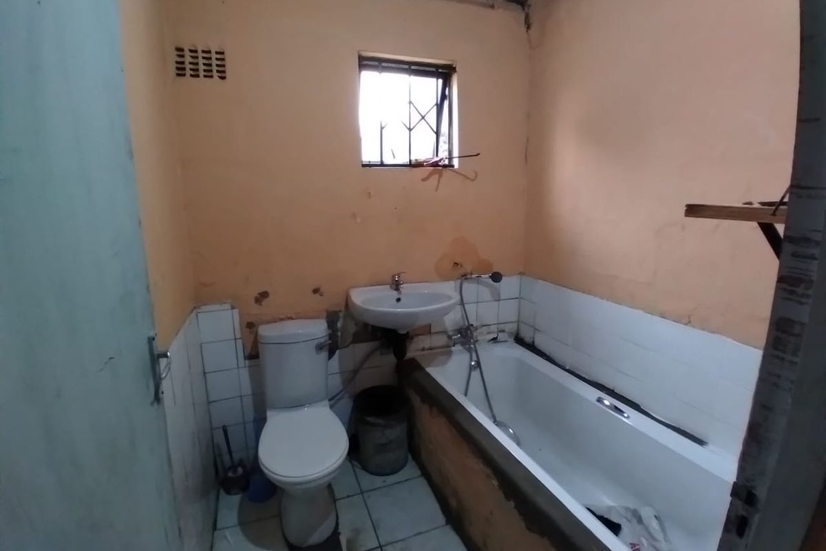A dated bathroom featuring a standard bathtub, wall-mounted basin, and toilet, requiring significant renovation and cosmetic repairs to the walls and ceiling.