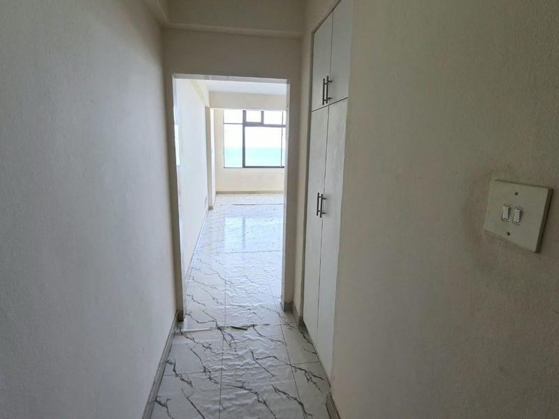 A vacant hallway featuring built-in storage cupboards and marble-look floor tiles, leading towards an open living area with natural light.