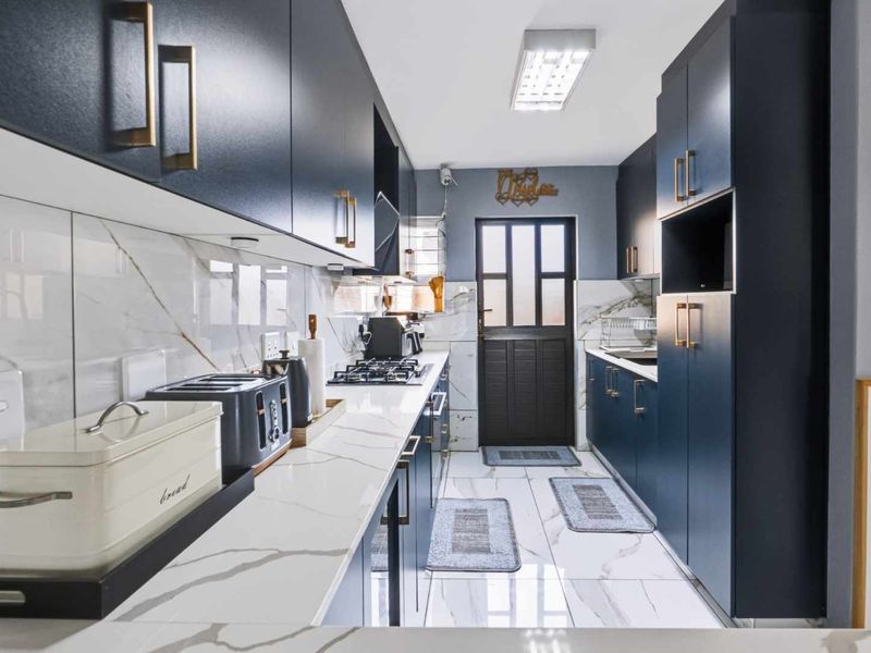 Modern galley-style kitchen featuring navy blue cabinetry, marble-look quartz countertops, high-end finishes, and a gas hob with integrated extractor.