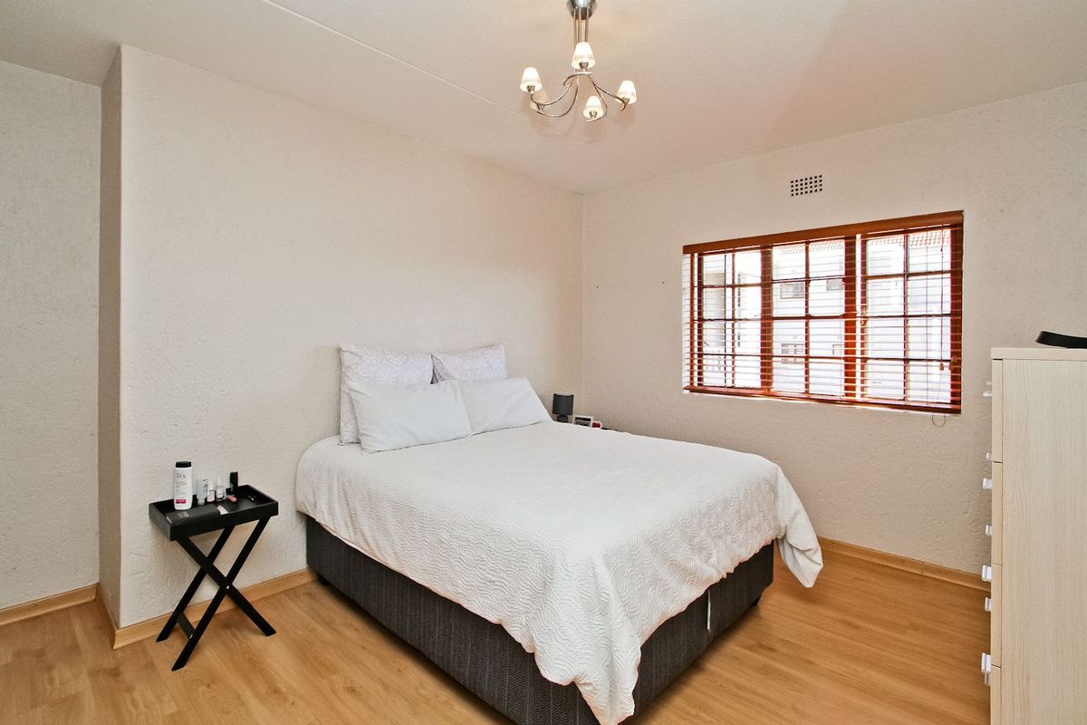 A well-maintained bedroom featuring light wood-look laminate flooring, textured walls, and a window fitted with wooden blinds.