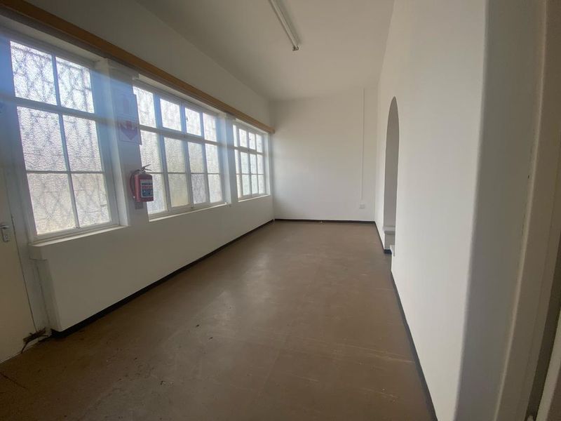 An empty, sunlit office space featuring large multi-pane windows, neutral walls, and an arched entryway, suitable for a variety of commercial uses.