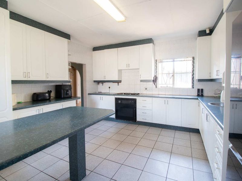 A functional kitchen featuring white cabinetry, dark laminate countertops, built-in oven and hob, and tiled flooring, offering a practical layout for daily use.