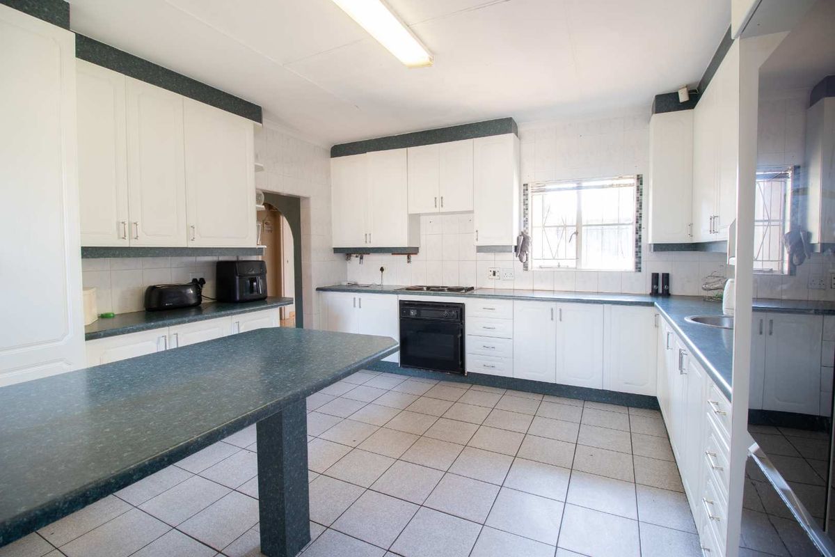 A functional kitchen featuring white cabinetry, dark laminate countertops, built-in oven and hob, and tiled flooring, offering a practical layout for daily use.