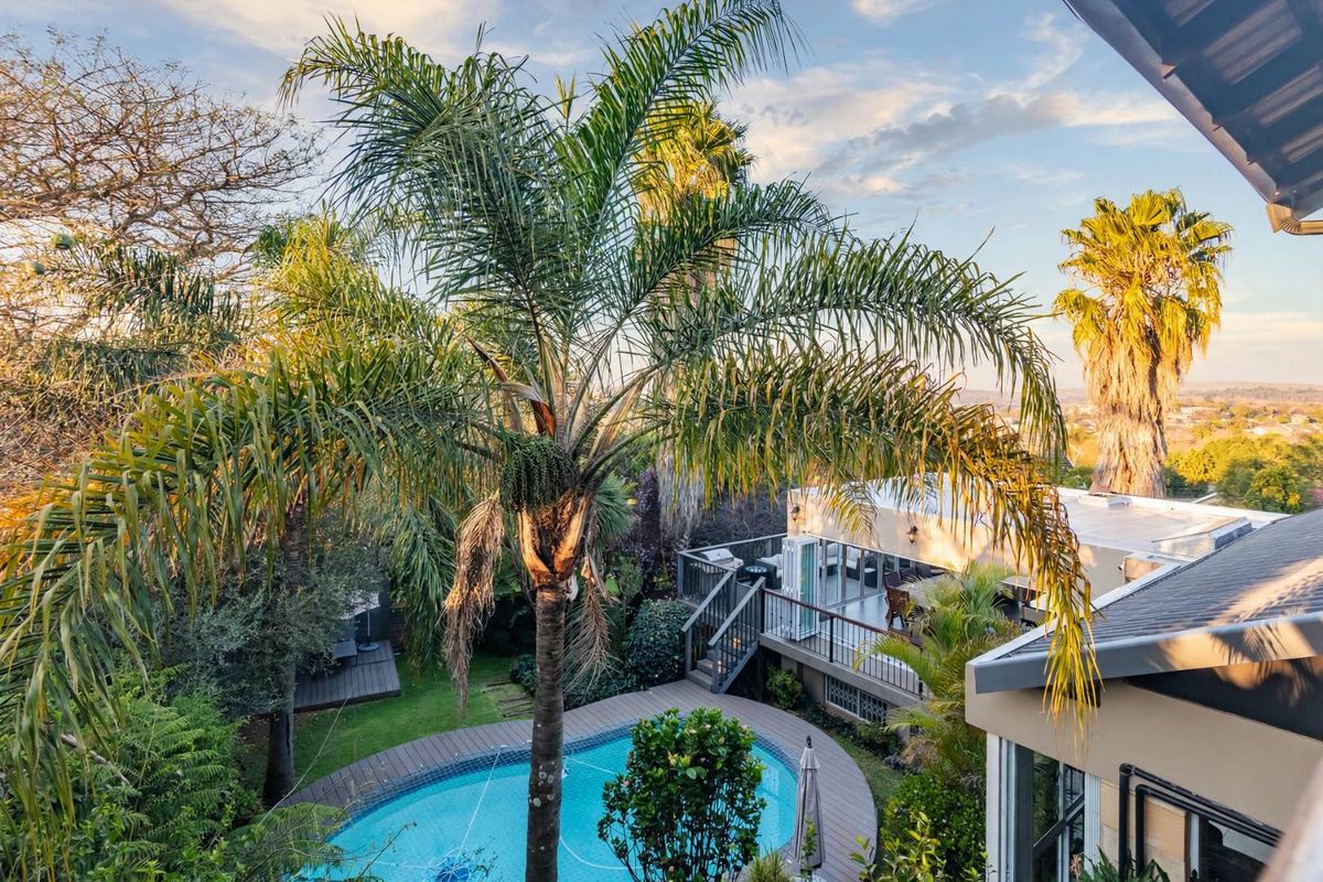 Elevated view of a landscaped backyard featuring a swimming pool, timber decking, and a raised patio area with access to the main dwelling.
