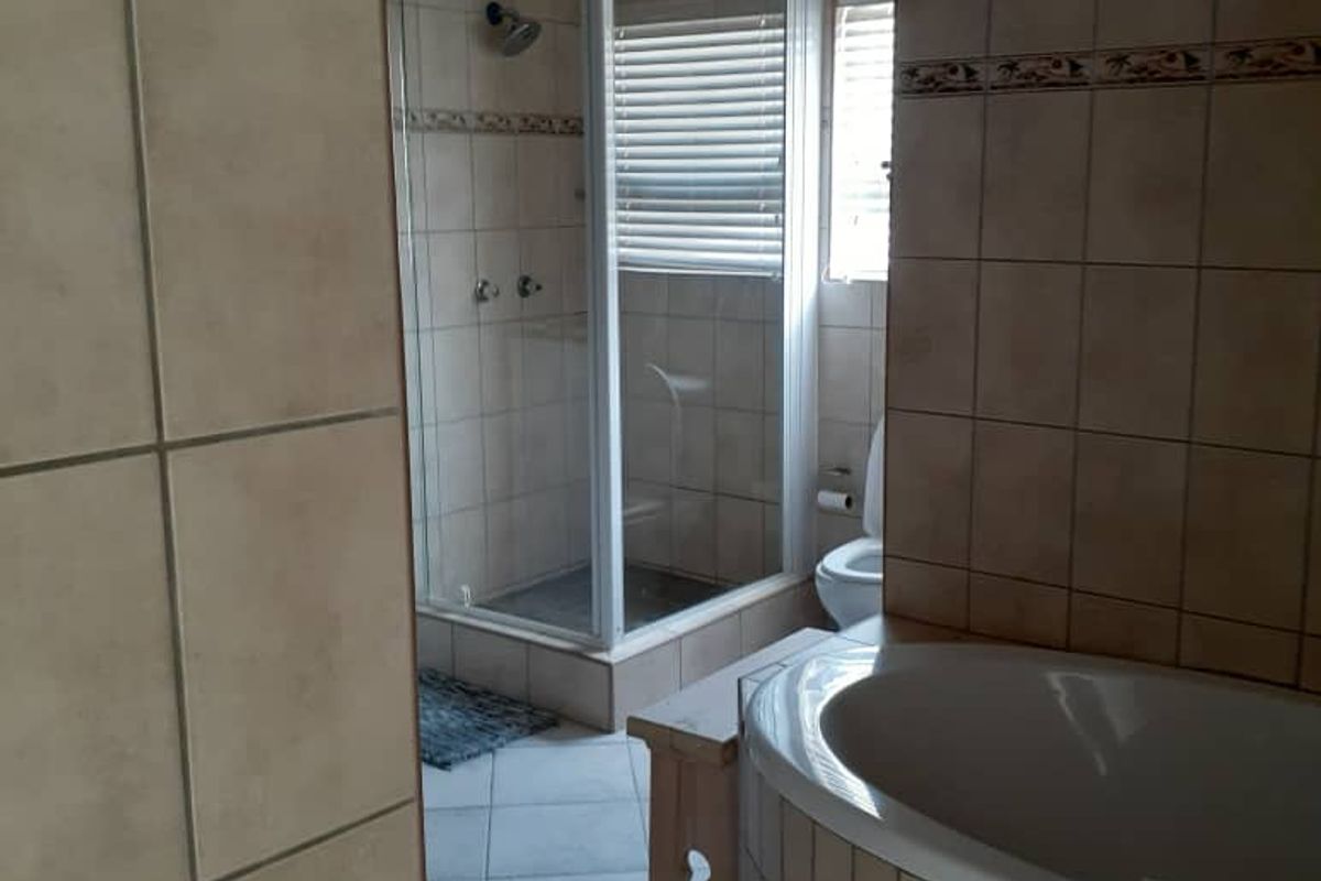A functional bathroom featuring a corner bathtub, a separate glass-enclosed shower, and neutral wall tiling throughout.