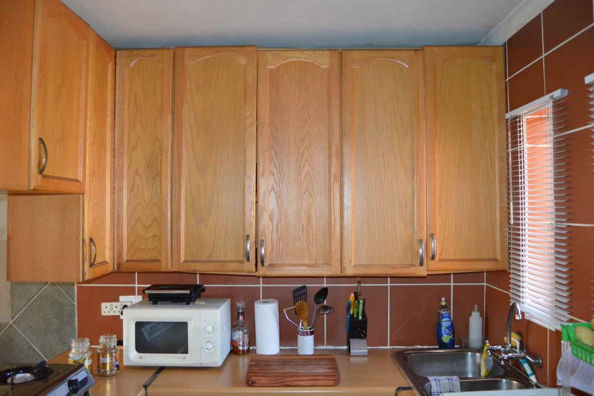 A functional kitchen featuring wooden cabinetry, a laminate countertop, a stainless steel double sink with a mixer tap, and a tiled backsplash.