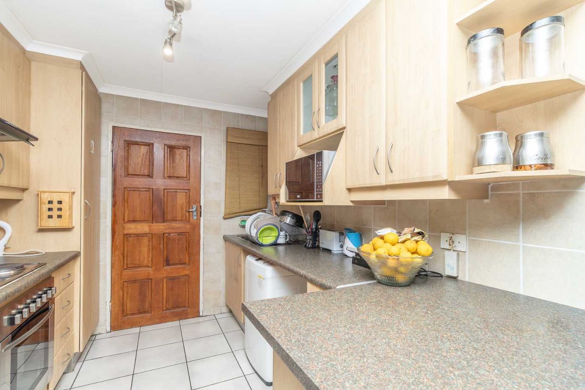 A functional kitchen featuring light wood cabinetry, tiled flooring, stone-look laminate countertops, and a built-in oven with extractor fan.