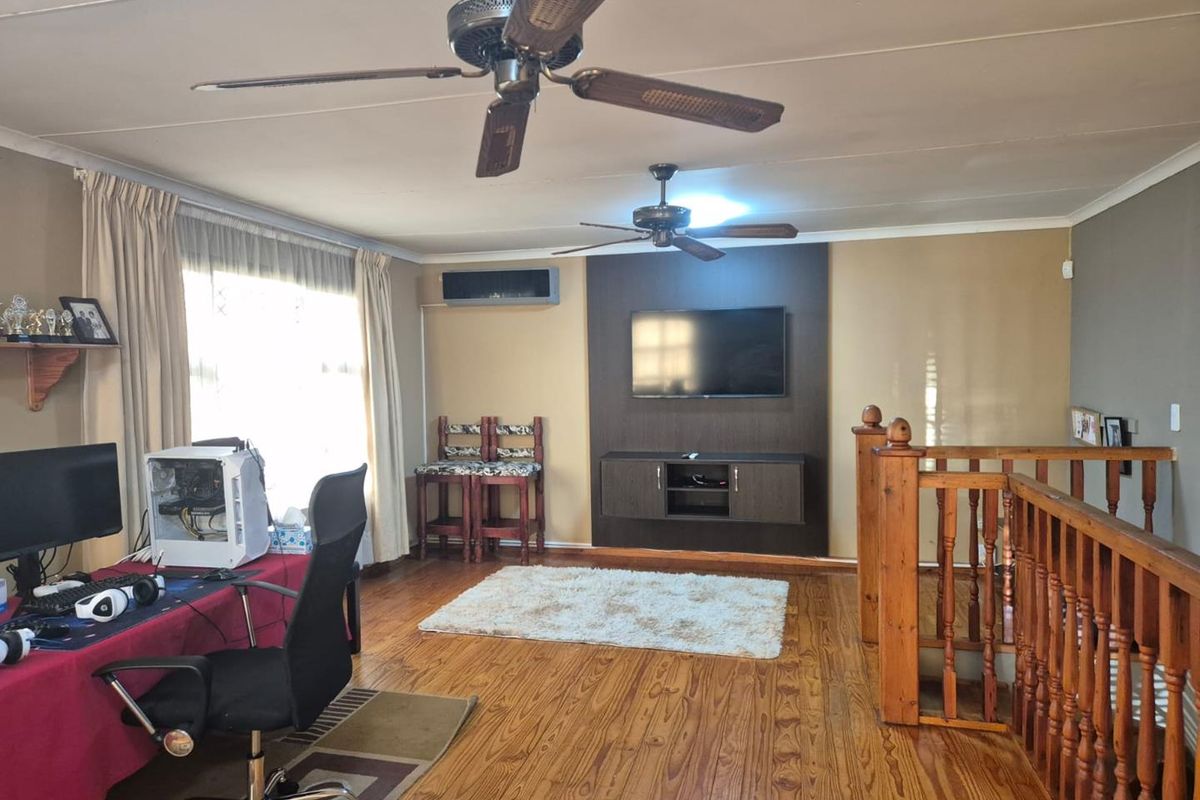 Spacious living area featuring timber flooring, dual ceiling fans, a split-system air conditioner, and a built-in media wall with a timber balustrade staircase.