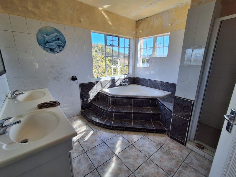A dated bathroom featuring a double vanity, corner bathtub with tiled steps, and a separate shower enclosure, requiring ceiling and finish repairs.