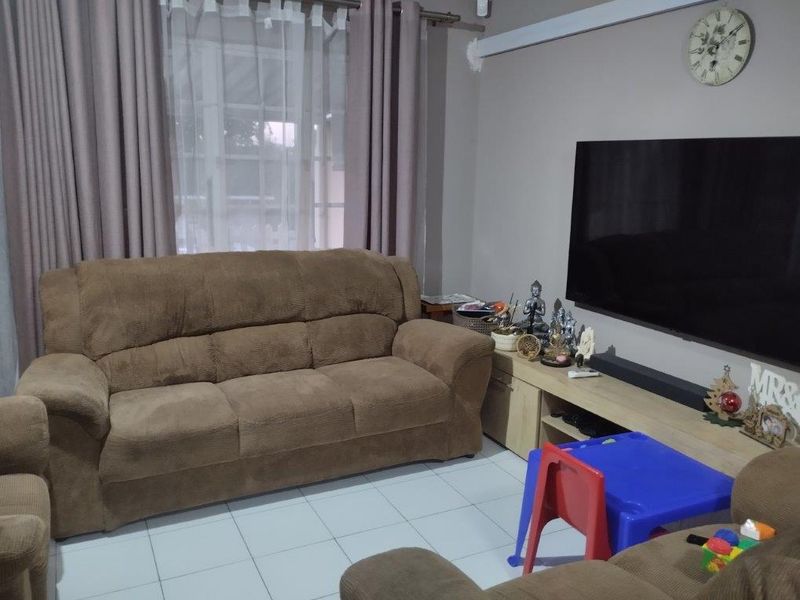 A comfortable living room featuring tiled flooring and large windows with curtain tracks, providing a functional space for relaxation.
