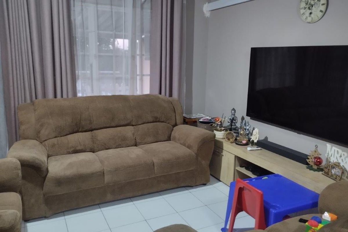 A comfortable living room featuring tiled flooring and large windows with curtain tracks, providing a functional space for relaxation.