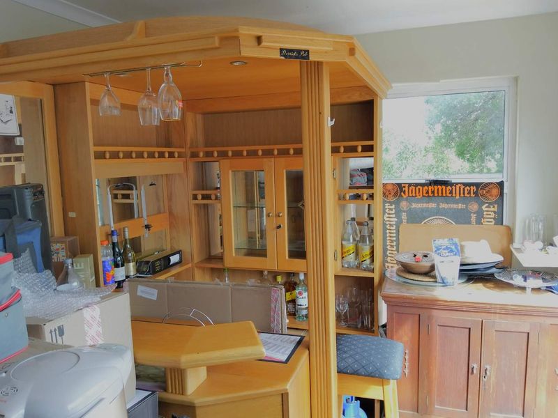 A dedicated home bar area featuring a built-in wooden bar unit with integrated glass display cabinets and overhead glass storage.