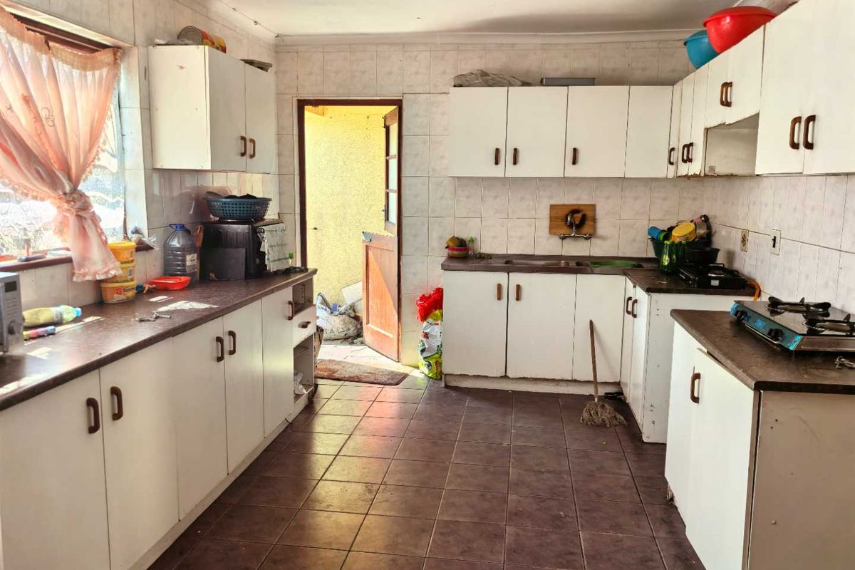 A dated kitchen featuring white cabinetry, tiled walls, and dark floor tiles, with direct access to an exterior area.