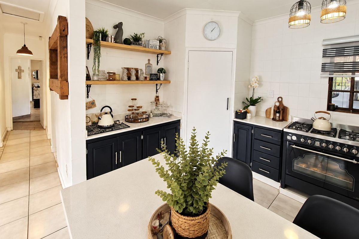 Modern kitchen featuring dark cabinetry, stone countertops, a gas stove with oven, and open shelving, complemented by tiled splashbacks and stylish pendant lighting.