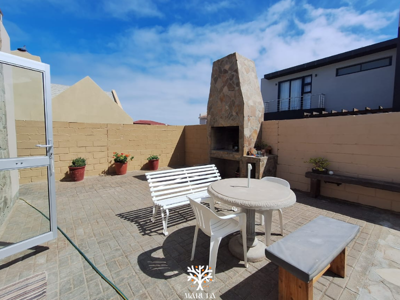 A paved outdoor patio area featuring a built-in stone fireplace and masonry boundary walls, providing a functional space for outdoor entertaining.