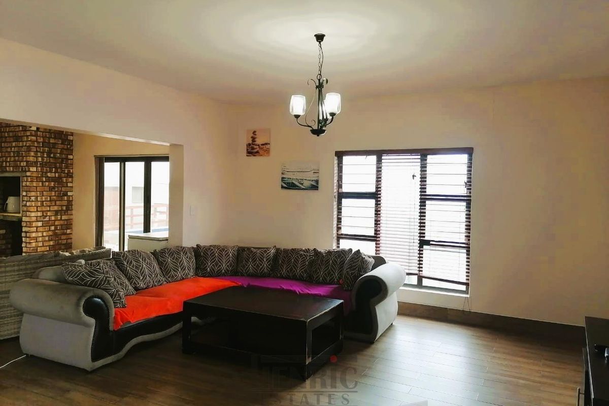 Spacious living room featuring laminate flooring, an exposed brick accent wall, and large windows allowing for natural light.