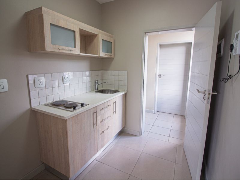Compact kitchen area featuring light wood cabinetry, a built-in electric hob, stainless steel sink, and neutral tiled flooring.