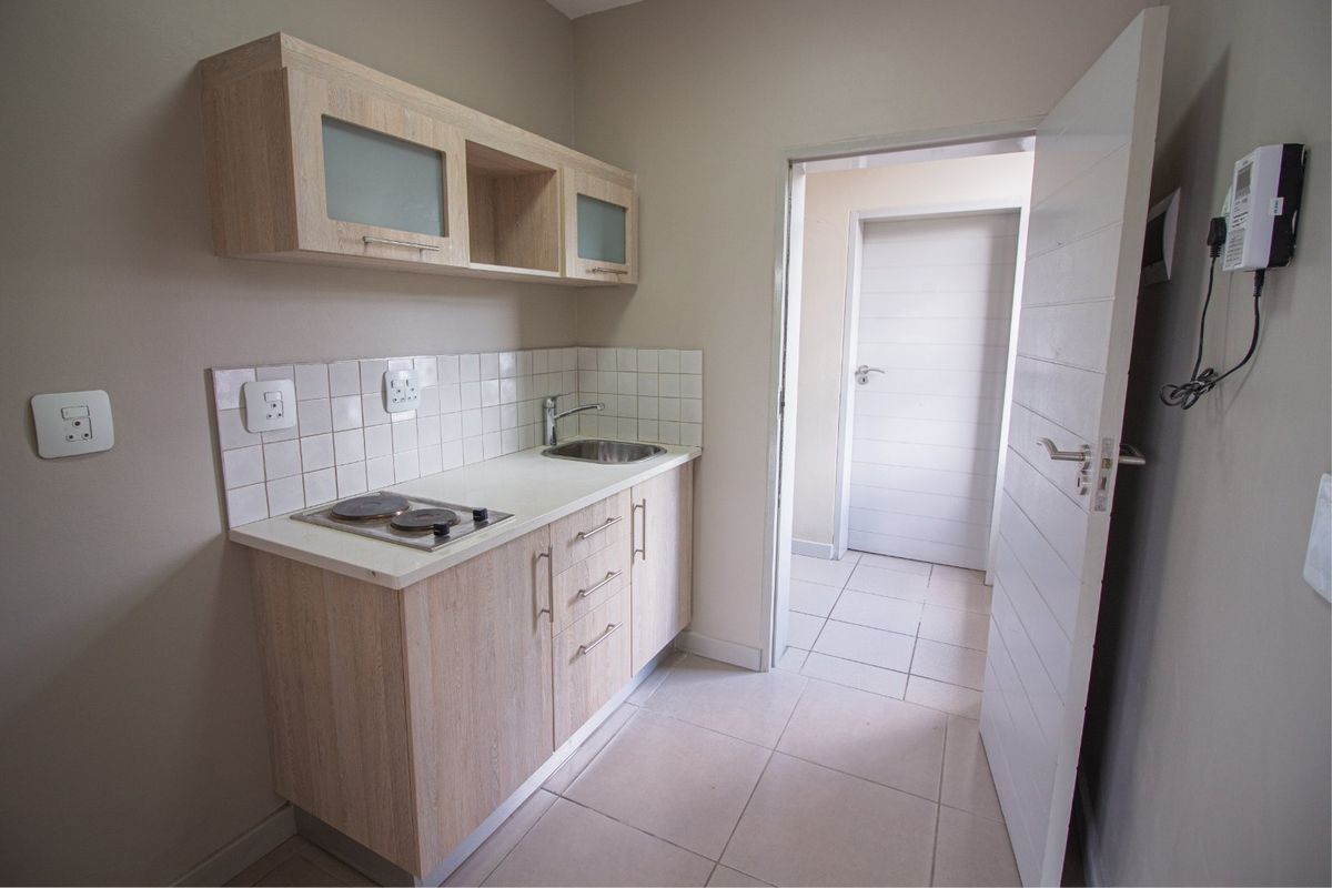 Compact kitchen area featuring light wood cabinetry, a built-in electric hob, stainless steel sink, and neutral tiled flooring.
