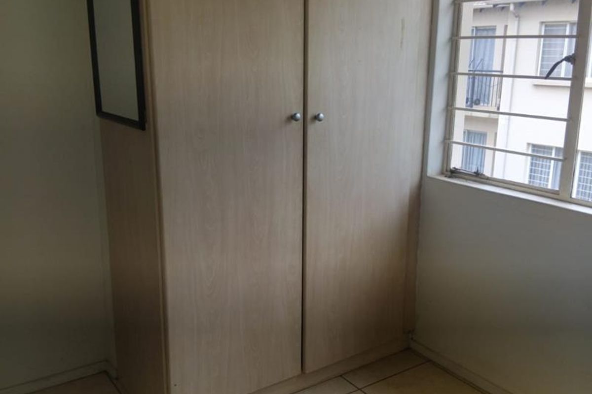A bedroom featuring built-in light wood-finish cabinetry and tiled flooring, with a window fitted with security bars.