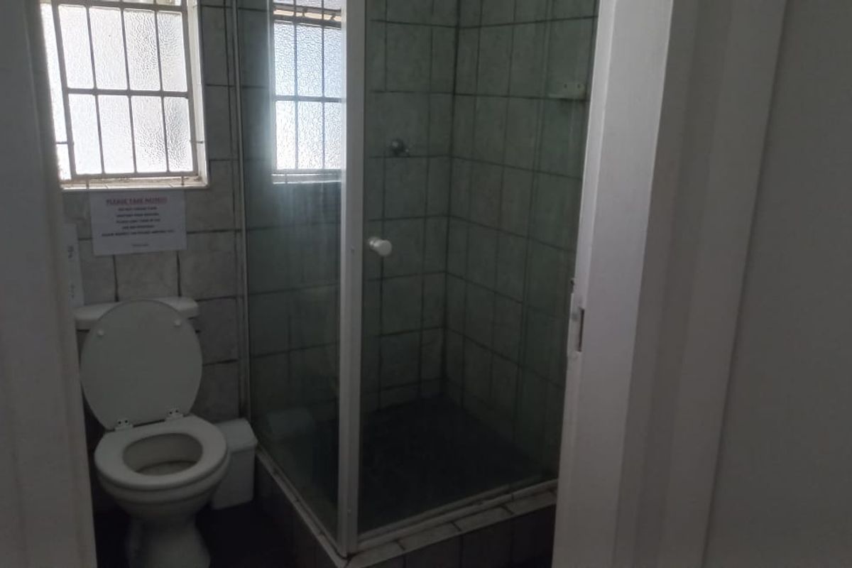 A compact bathroom featuring a corner shower enclosure with glass doors and a standard toilet, finished with dated wall tiles and security bars on windows.