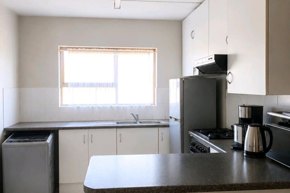 A functional kitchen featuring white cabinetry, laminate countertops, tiled flooring, and a built-in extractor fan, offering a clean and practical workspace.