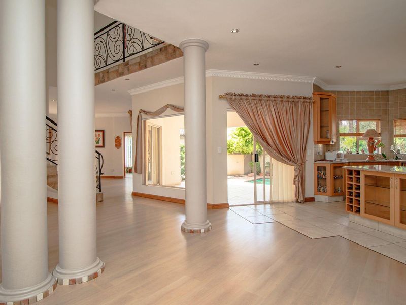 Spacious open-plan living area featuring structural columns, a grand staircase with wrought iron railings, and a functional kitchen with built-in cabinetry.