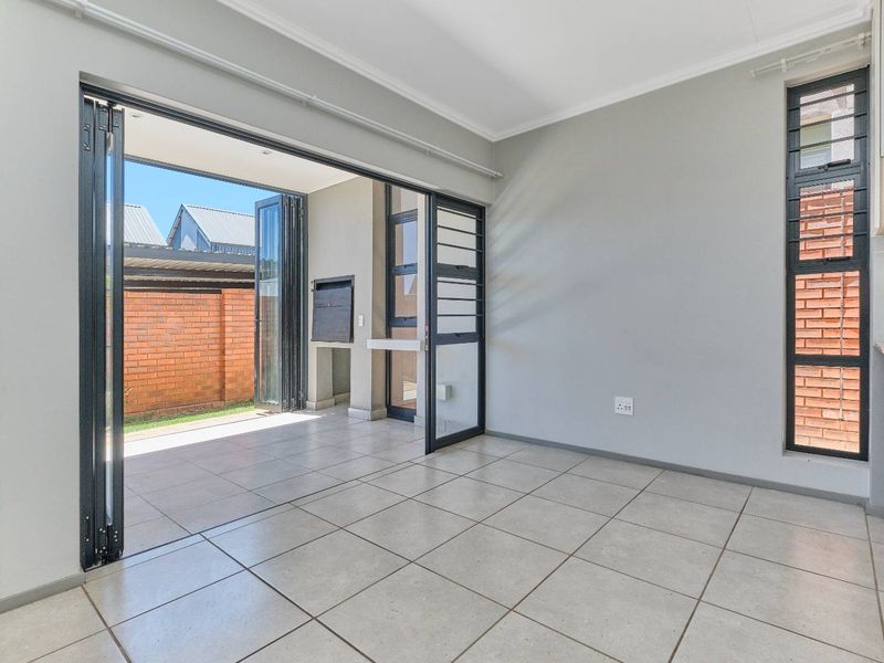 Open-plan living area featuring tiled floors, modern stacking doors leading to a patio with a built-in braai, and neutral wall finishes.