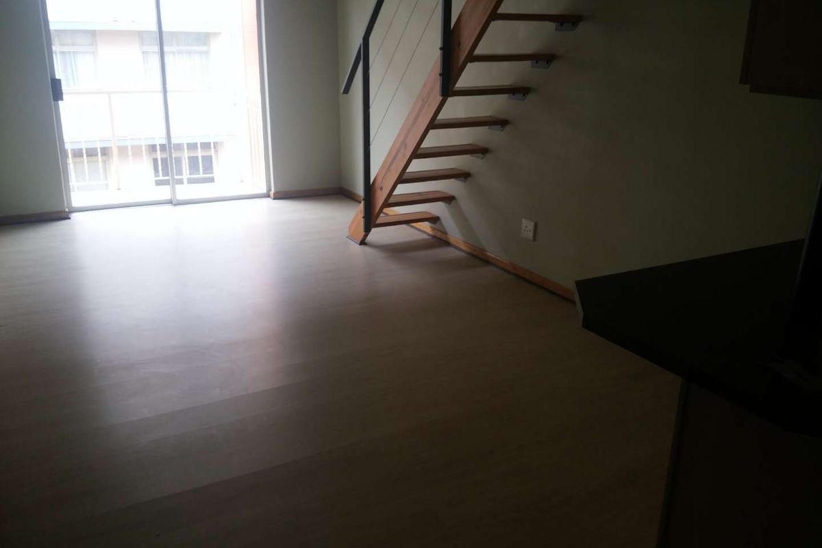 Open plan living area featuring a timber staircase with metal handrail and sliding glass doors leading to a balcony.