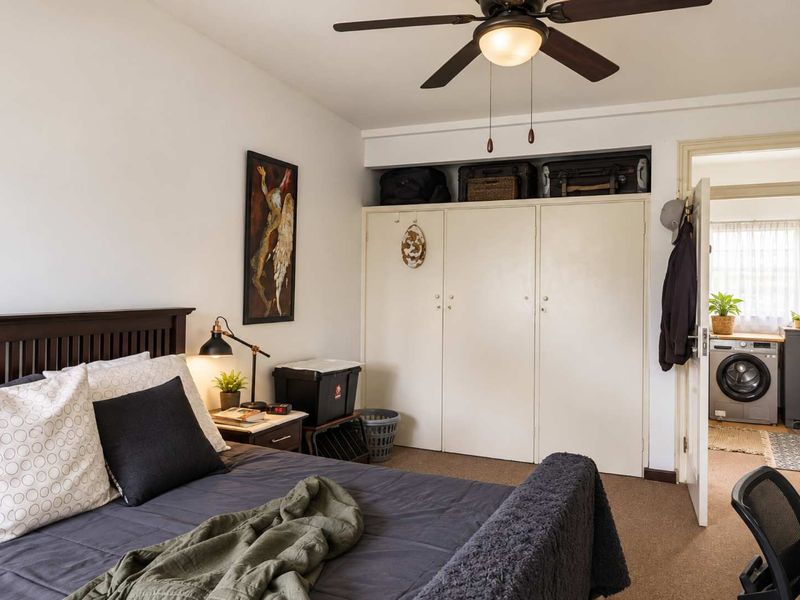 A bedroom featuring built-in cupboards, a ceiling fan, and carpet flooring, with an adjacent view into a laundry area.