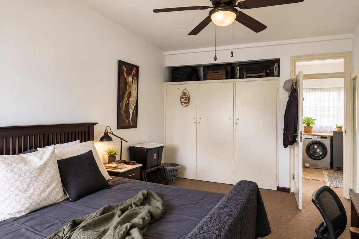 A bedroom featuring built-in cupboards, a ceiling fan, and carpet flooring, with an adjacent view into a laundry area.