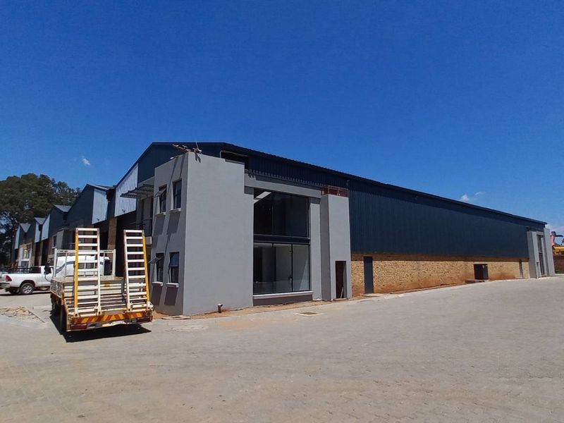 Exterior view of an industrial warehouse facility featuring metal cladding, brickwork, and a large paved yard area suitable for logistics or manufacturing operations.