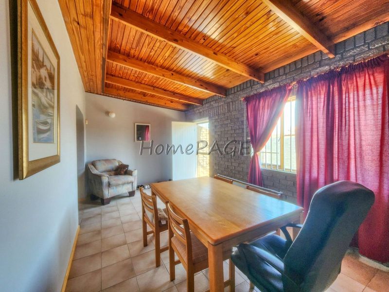 Dining room featuring a rustic exposed timber beam ceiling, tiled flooring, and an exposed brick feature wall with natural light.