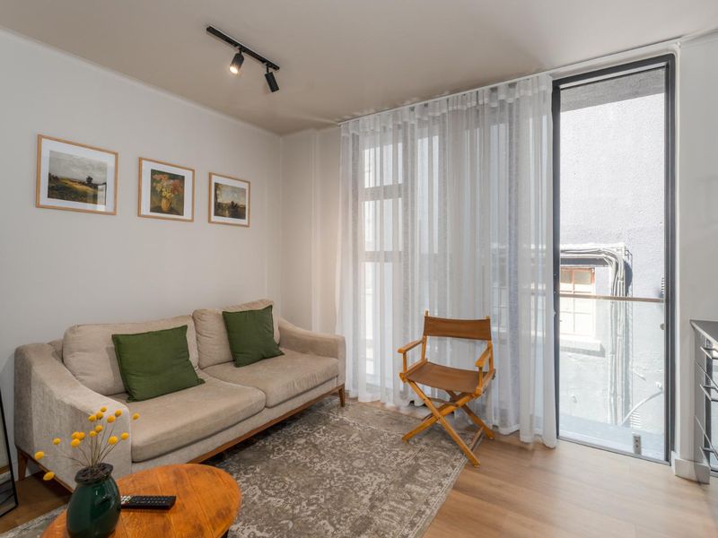 Bright open-plan living area featuring modern track lighting, laminate flooring, and direct access to a private balcony through a large sliding glass door.