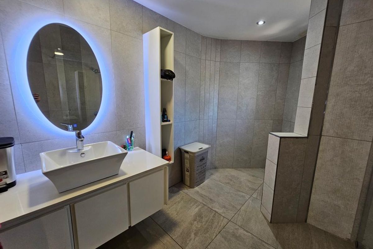 Modern bathroom featuring a vessel sink vanity, illuminated oval mirror, built-in shelving, and large-format floor and wall tiling.