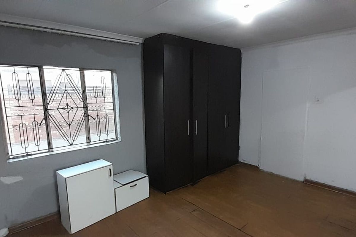 A bedroom featuring built-in cupboards, wooden flooring, and security bars on the window.