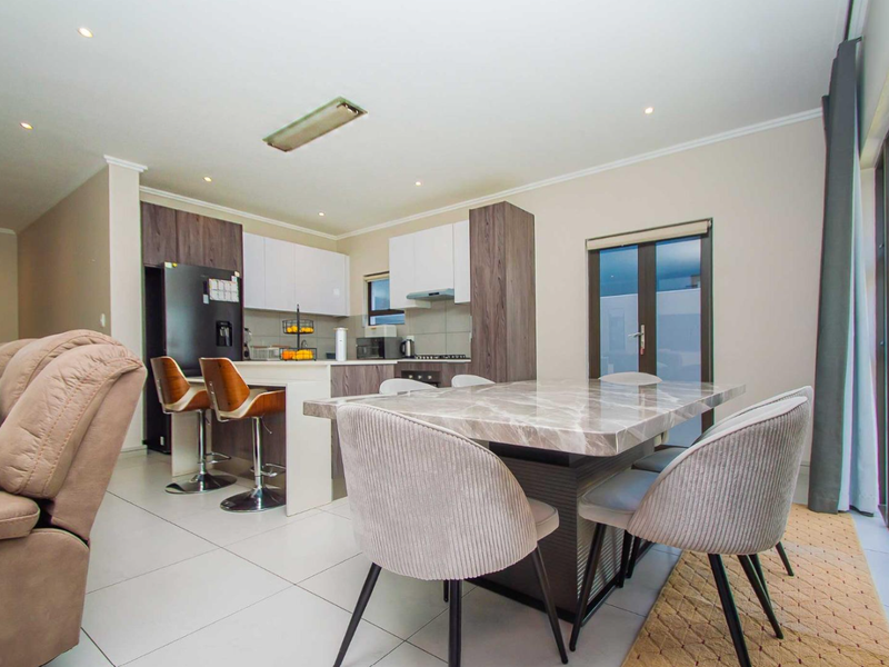 Modern open-plan kitchen and dining area featuring sleek cabinetry, a stone-topped island, tiled floors, and direct access to the outdoors via sliding glass doors.