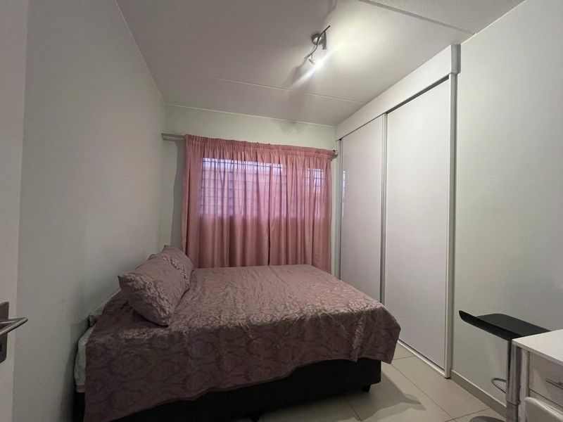 A functional bedroom featuring tiled flooring, a built-in sliding door wardrobe, and a window with curtain treatments.
