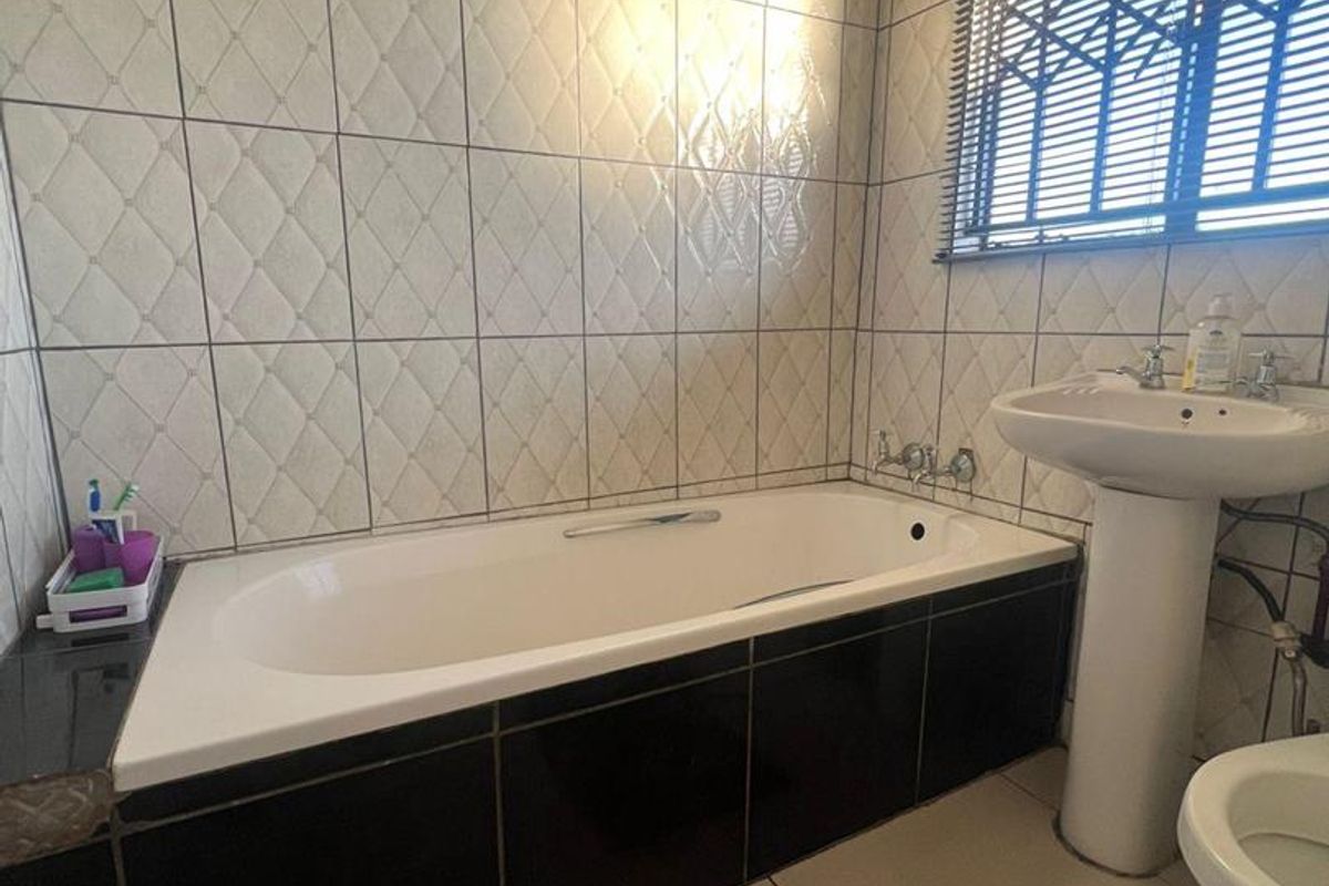 A functional bathroom featuring a built-in bathtub with black tiling, a pedestal basin, and textured wall tiles.