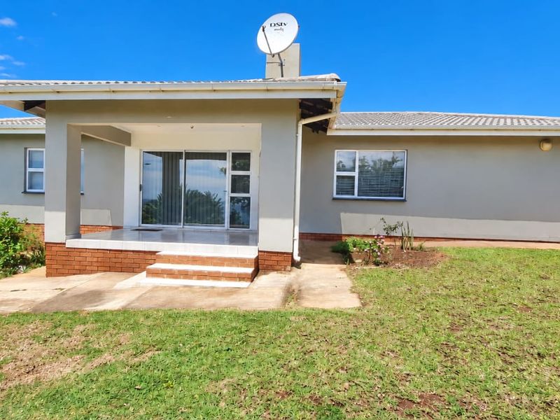 Rear view of the cluster home featuring a covered patio, sliding glass doors, and a spacious garden area with a concrete walkway.