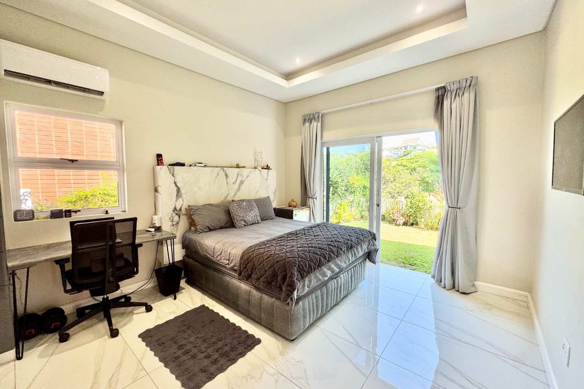 Spacious bedroom featuring modern marble-look floor tiles, a recessed ceiling with downlights, a wall-mounted air conditioning unit, and sliding glass doors opening to the garden.