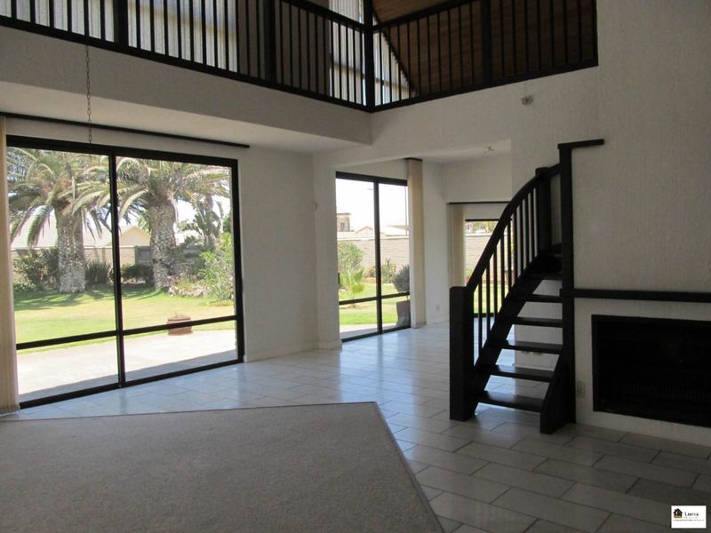 Spacious double-volume living area featuring a fireplace, staircase to a mezzanine level, and large sliding glass doors opening to the garden.