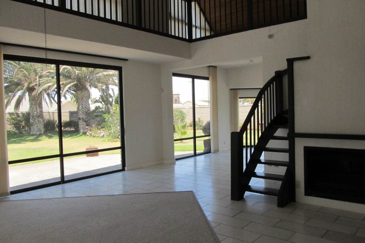 Spacious double-volume living area featuring a fireplace, staircase to a mezzanine level, and large sliding glass doors opening to the garden.