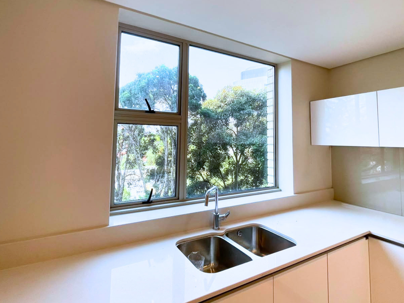 A modern, minimalist kitchen featuring sleek white handleless cabinetry, a double bowl stainless steel sink, and a clean quartz countertop with a glass splashback.