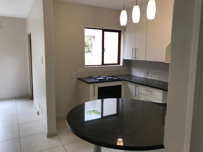 Modern kitchen featuring white cabinetry, dark granite countertops, built-in oven and hob, subway tile backsplash, and a breakfast bar island.