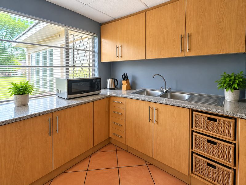 A functional kitchen featuring light wood cabinetry, granite countertops, a stainless steel double sink, and tiled flooring with natural light from the window.