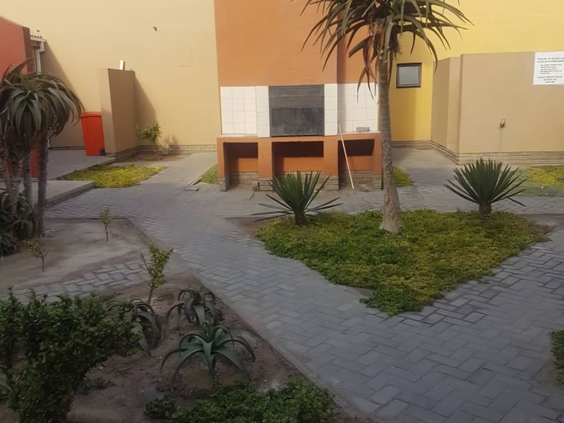 Rear courtyard area featuring a built-in braai, paved pathways, and established garden beds within a residential apartment complex.